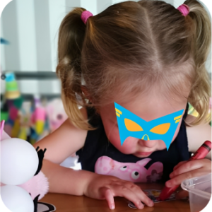 Child in blue mask coloring at table